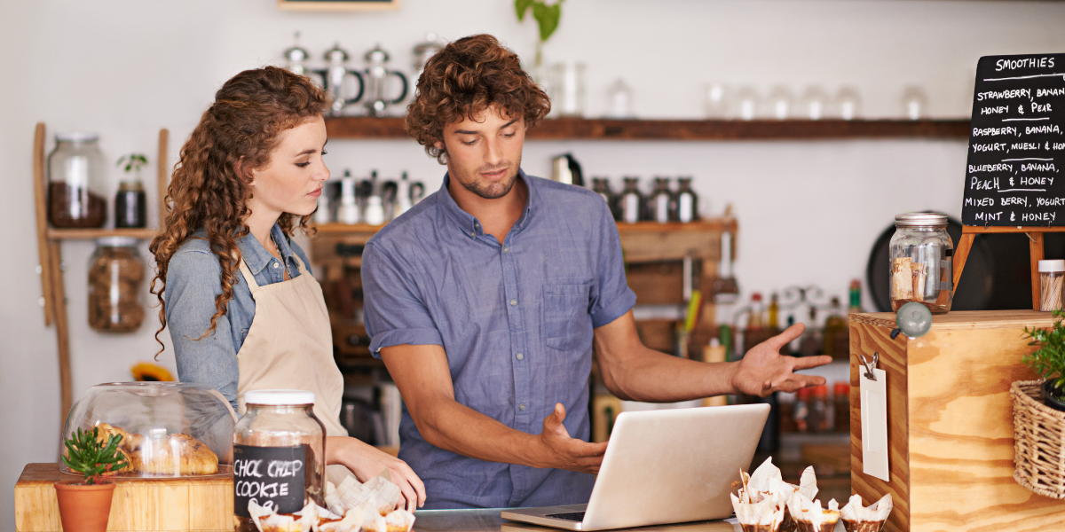 Employees talking over a computer behind the counter of a shop. 